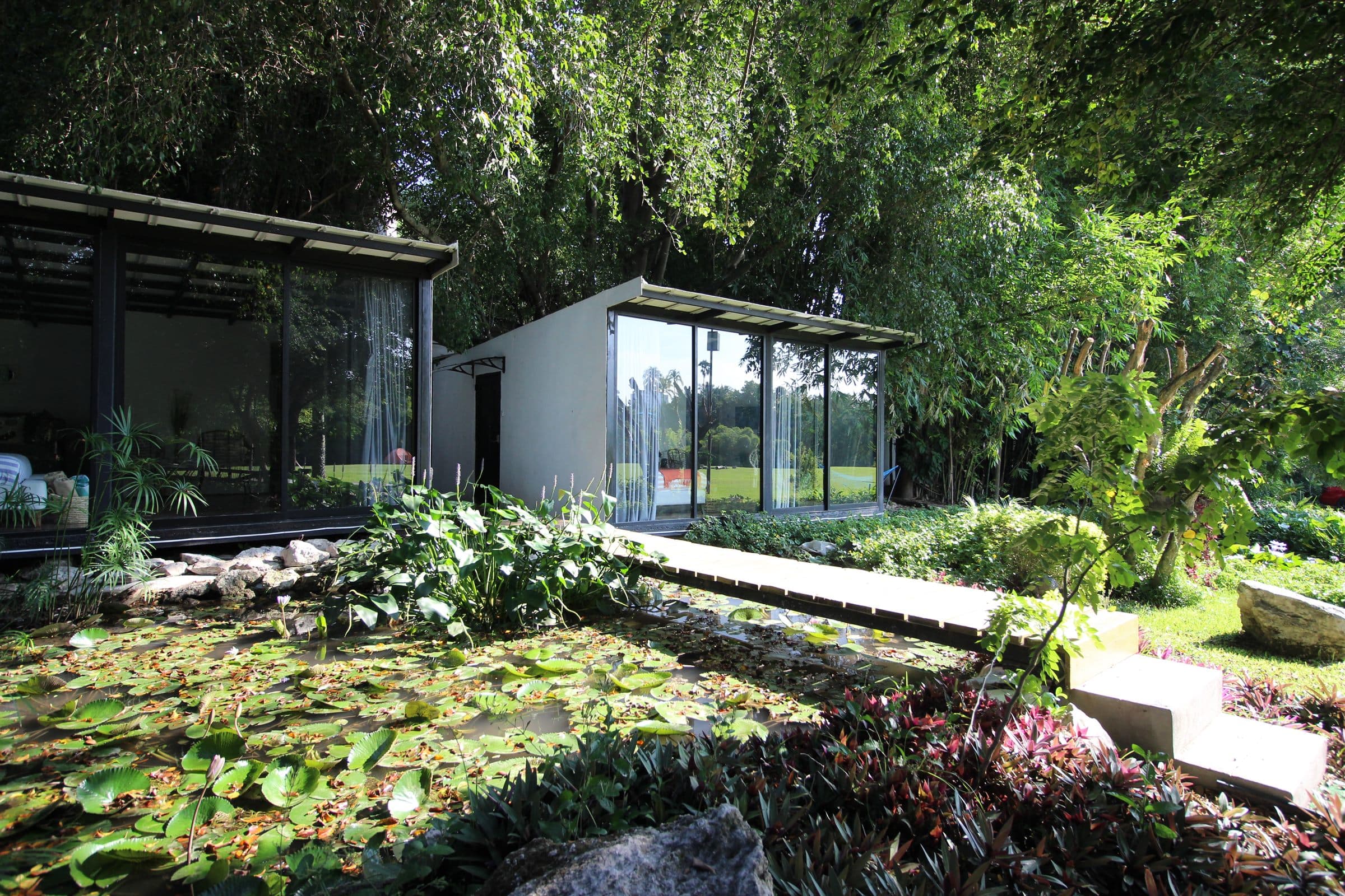 Las habitaciones de cristal de Casa del Lago junto al estanque de nenúfares, con el puente de madera y los jardines