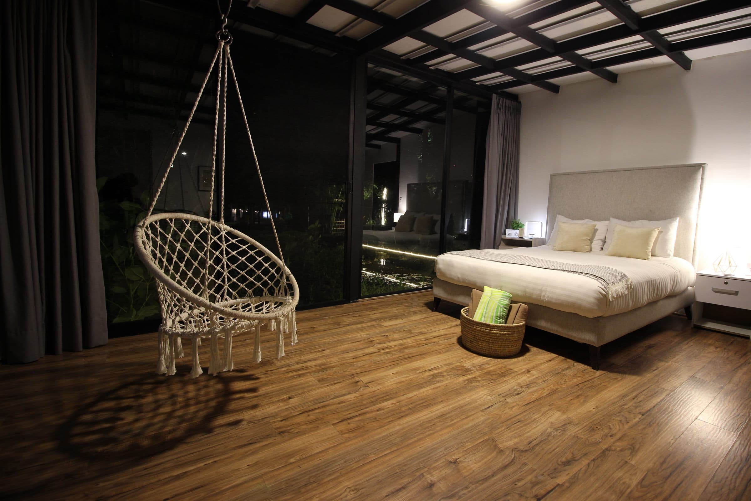 La habitación de noche, con luz cálida y el jardín iluminado detrás del cristal